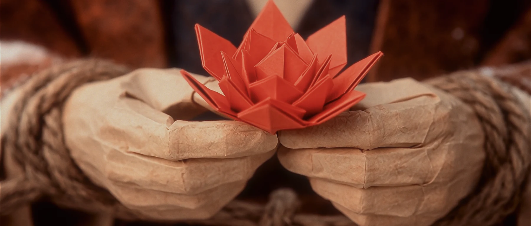 Bound paper hands holding a small red folded flower